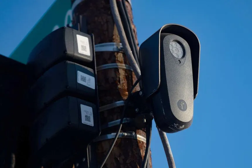 Close-up of a Flock Safety license plate reader camera on a wooden pole, showing the hooded lens and infrared illuminator